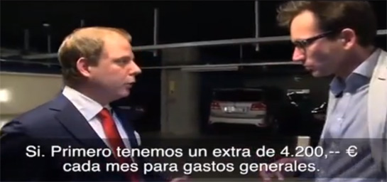 hombre rubio de traje y corbata roja hablando con otro hombre en un aparcamiento subterráneo